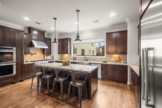 kitchen with stainless steel appliances, light stone counters, decorative backsplash, a breakfast bar, and a kitchen island