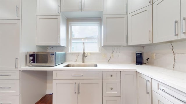 kitchen featuring light stone counters, white cabinetry, sink, and tasteful backsplash