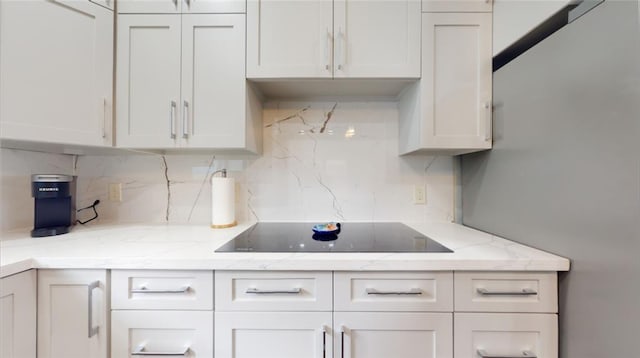 kitchen featuring white cabinets, light stone countertops, black electric cooktop, and tasteful backsplash