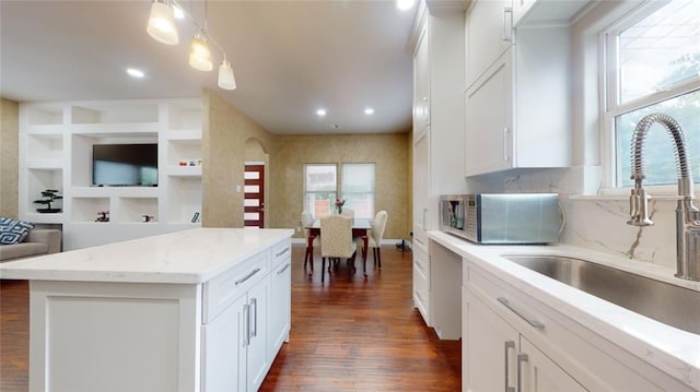 kitchen featuring white cabinetry, a center island, sink, built in features, and pendant lighting