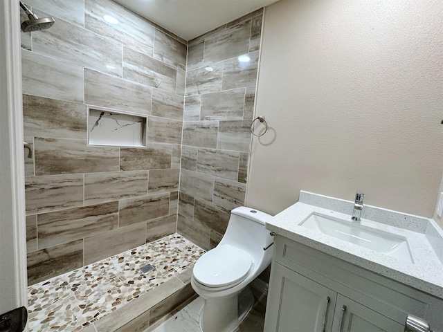 bathroom with a tile shower, vanity, and toilet