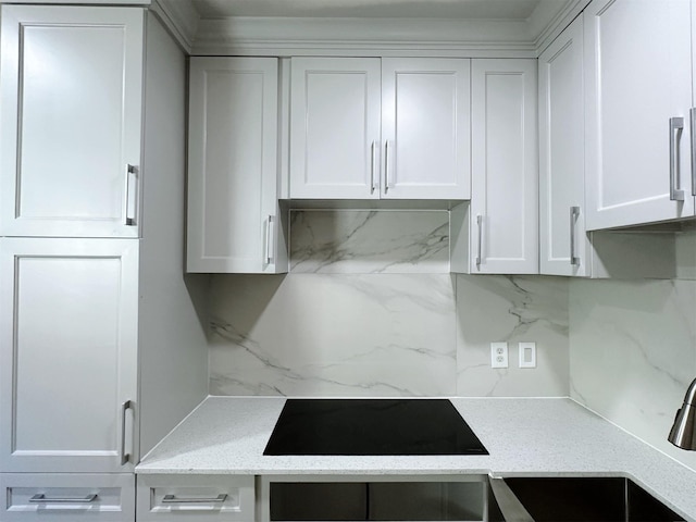 kitchen featuring light stone countertops, tasteful backsplash, black electric cooktop, sink, and white cabinets