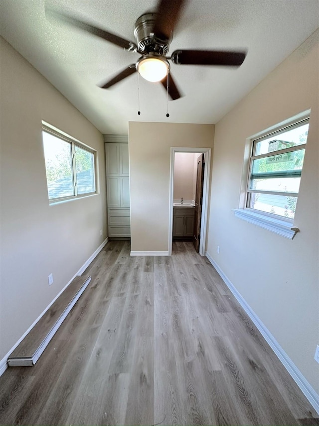 unfurnished bedroom featuring a textured ceiling, light wood-type flooring, ensuite bathroom, and ceiling fan