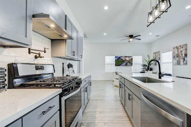 kitchen featuring sink, gray cabinetry, hanging light fixtures, appliances with stainless steel finishes, and wall chimney range hood