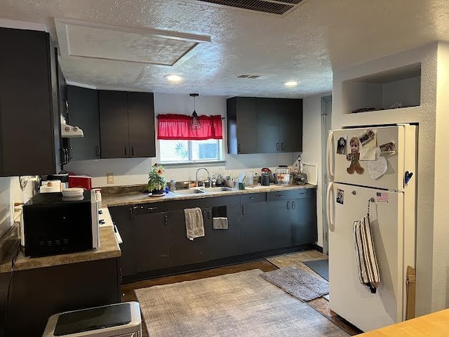 kitchen featuring a textured ceiling, white fridge, hanging light fixtures, and sink