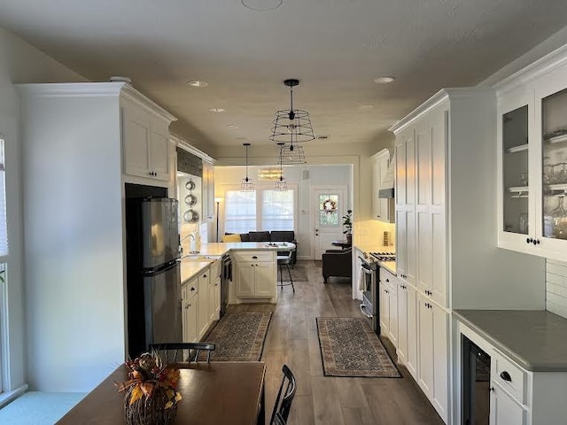 kitchen featuring kitchen peninsula, appliances with stainless steel finishes, decorative light fixtures, a kitchen bar, and white cabinetry