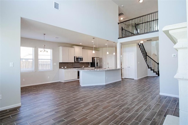 kitchen featuring decorative backsplash, appliances with stainless steel finishes, a kitchen island with sink, white cabinetry, and hanging light fixtures