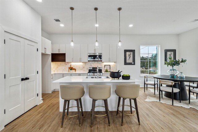 kitchen with stainless steel appliances, a center island with sink, hanging light fixtures, and white cabinetry