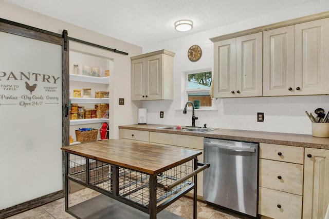 kitchen with sink, a barn door, stainless steel dishwasher, cream cabinets, and light tile patterned flooring