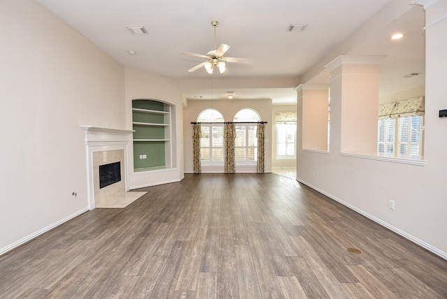 unfurnished living room featuring ceiling fan, plenty of natural light, built in features, and a tile fireplace