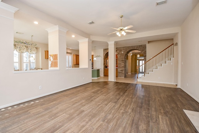 unfurnished living room with hardwood / wood-style flooring, ceiling fan with notable chandelier, and ornate columns