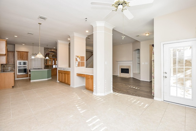 unfurnished living room with decorative columns, ceiling fan, sink, and light tile patterned floors