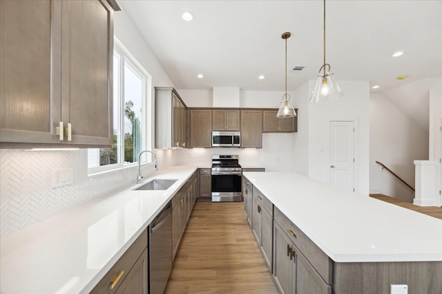 kitchen featuring light hardwood / wood-style floors, stainless steel appliances, a center island, sink, and decorative light fixtures