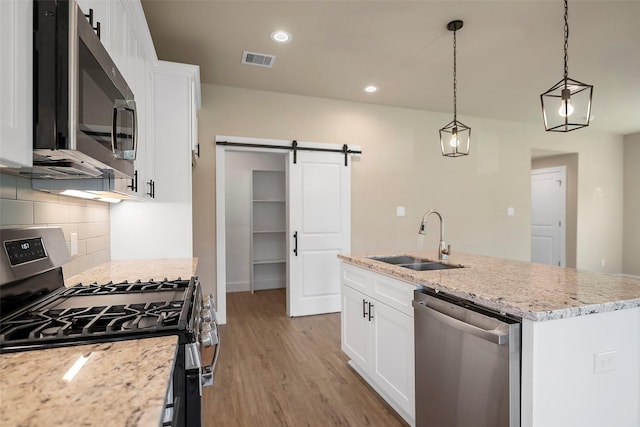 kitchen featuring sink, a barn door, an island with sink, appliances with stainless steel finishes, and white cabinetry