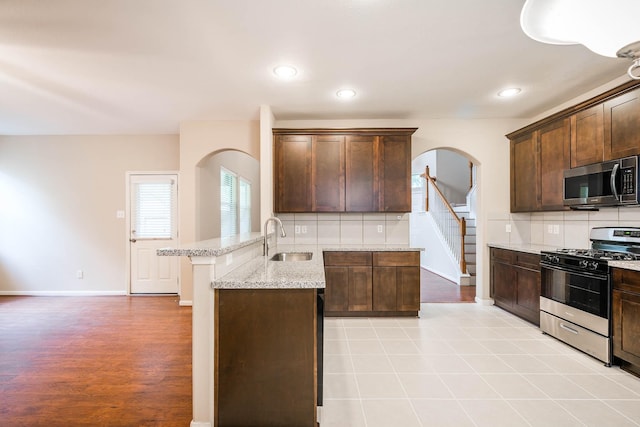 kitchen with dark brown cabinetry, light stone countertops, sink, backsplash, and appliances with stainless steel finishes