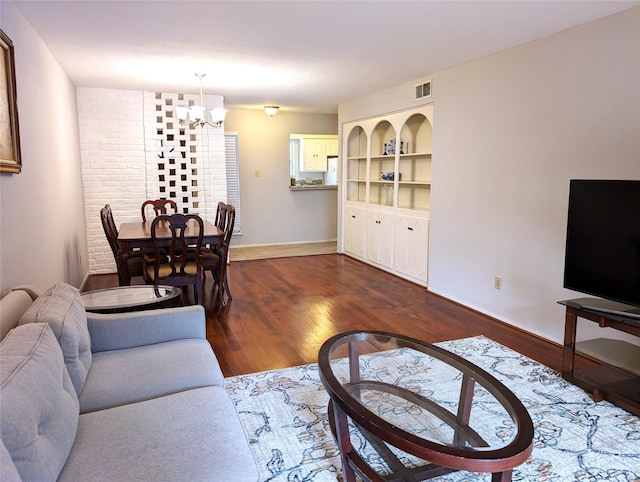 living room featuring built in features, dark hardwood / wood-style floors, and an inviting chandelier