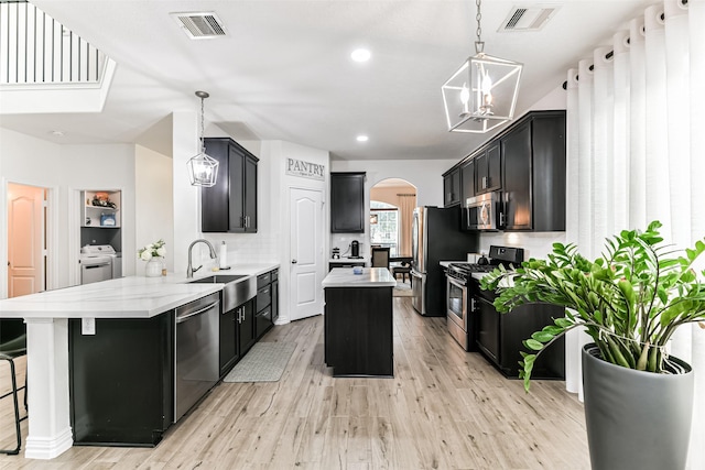 kitchen with appliances with stainless steel finishes, light wood-type flooring, decorative light fixtures, a chandelier, and independent washer and dryer