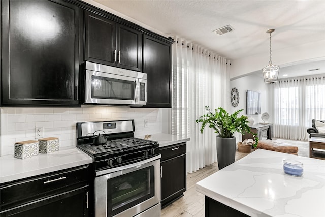 kitchen with pendant lighting, decorative backsplash, light wood-type flooring, appliances with stainless steel finishes, and light stone counters