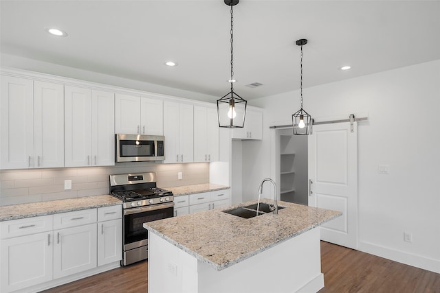 745 20th St, Hempstead, TX 77445 - kitchen featuring a barn door, white cabinetry, a kitchen island with sink, and appliances with stainless steel finishes