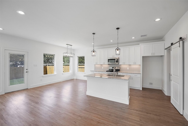 745 20th St, Hempstead, TX 77445 - kitchen featuring stainless steel appliances, a barn door, light stone counters, a center island with sink, and white cabinets
