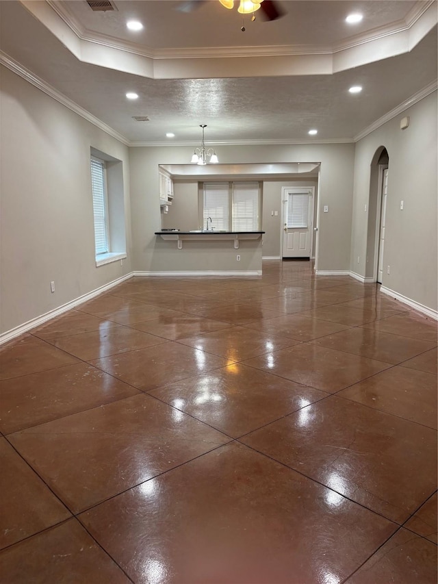 unfurnished living room with ceiling fan with notable chandelier, ornamental molding, sink, and a tray ceiling