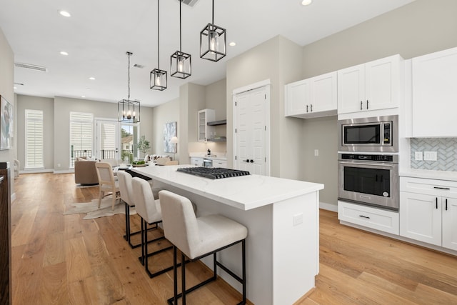 kitchen with white cabinetry, a center island, decorative light fixtures, decorative backsplash, and appliances with stainless steel finishes