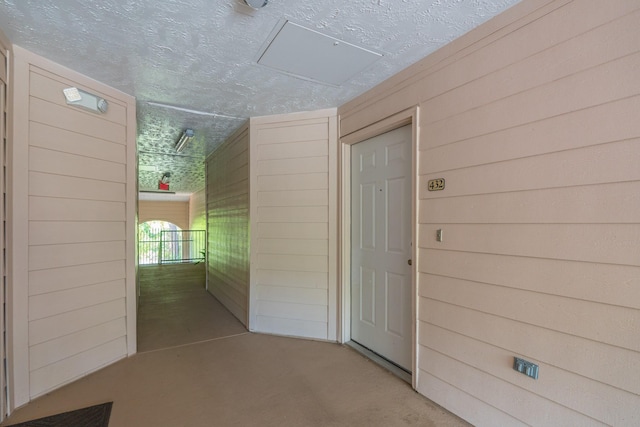 hall featuring wooden walls and a textured ceiling