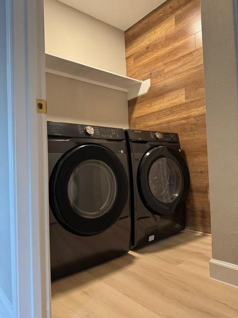 laundry area with wooden walls, light hardwood / wood-style flooring, and independent washer and dryer