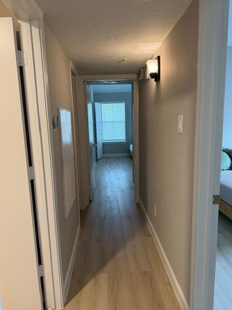 hall with a textured ceiling and light hardwood / wood-style flooring