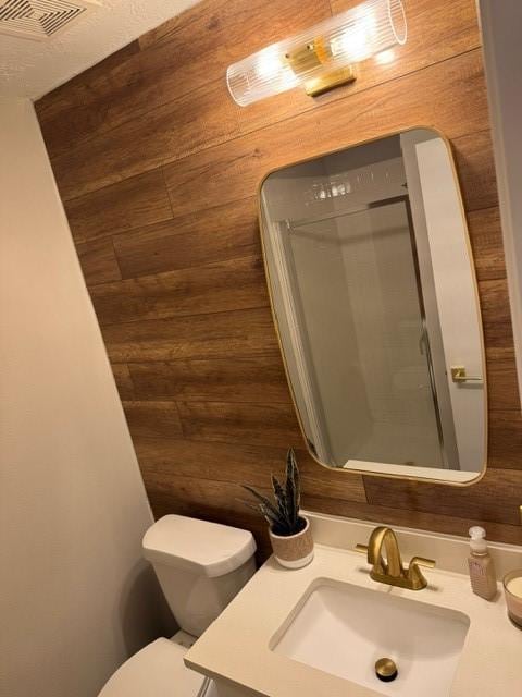 bathroom featuring vanity, toilet, and wood walls