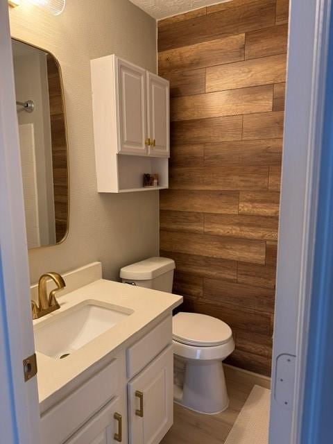 bathroom with vanity, wood walls, toilet, rustic walls, and wood-type flooring