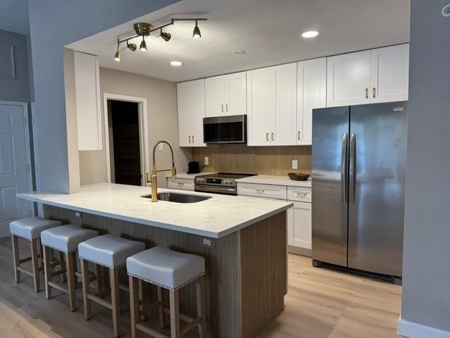 kitchen with white cabinetry, sink, stainless steel appliances, a kitchen breakfast bar, and light hardwood / wood-style flooring