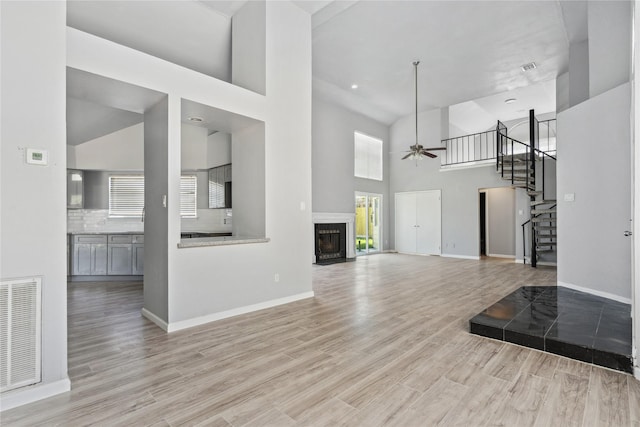 unfurnished living room featuring a high ceiling, light wood-type flooring, and ceiling fan