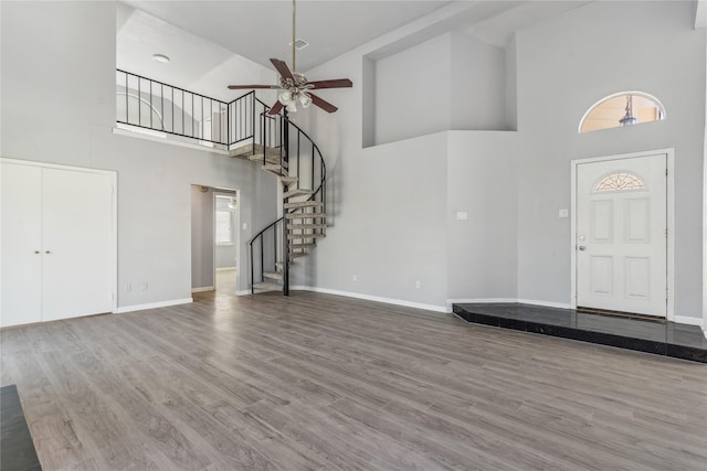 unfurnished living room with ceiling fan, wood-type flooring, and a high ceiling