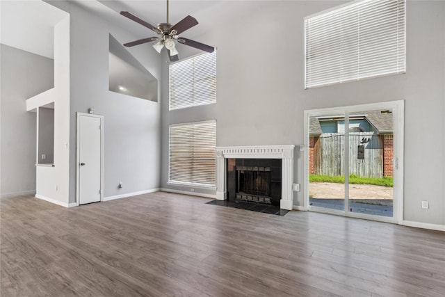 unfurnished living room with ceiling fan, wood-type flooring, a fireplace, and a high ceiling