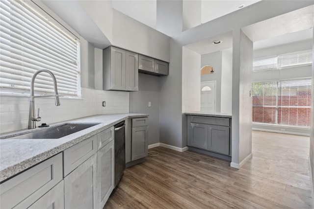 kitchen featuring decorative backsplash, stainless steel dishwasher, gray cabinetry, sink, and hardwood / wood-style floors