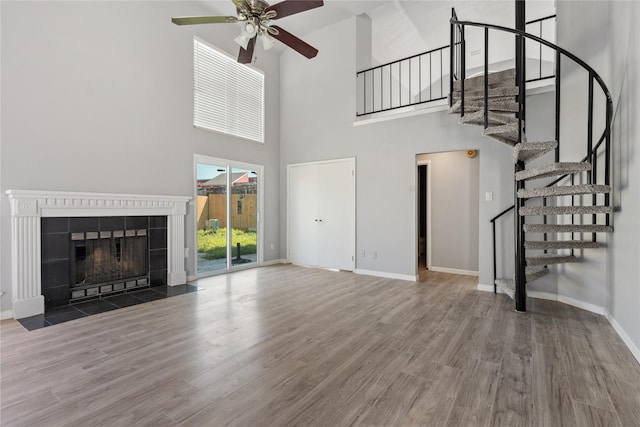 unfurnished living room featuring hardwood / wood-style floors, ceiling fan, a towering ceiling, and a tiled fireplace