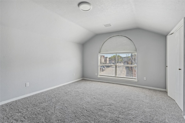 unfurnished room with a textured ceiling, carpet, and lofted ceiling