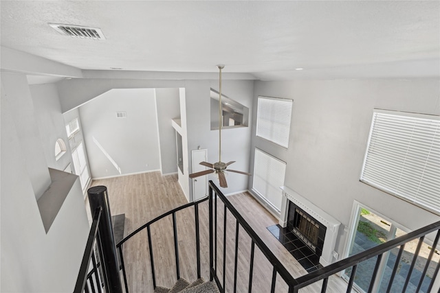 stairway with ceiling fan, hardwood / wood-style floors, a textured ceiling, lofted ceiling, and a fireplace