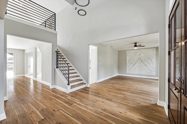 entrance foyer with ceiling fan, wood-type flooring, and a towering ceiling