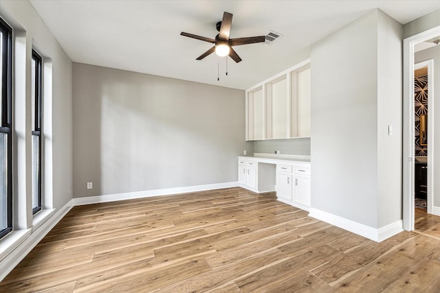 empty room with ceiling fan, light hardwood / wood-style flooring, and built in desk