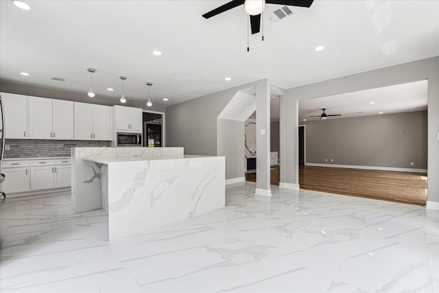 kitchen with light stone countertops, tasteful backsplash, white cabinets, a center island, and stainless steel microwave