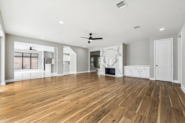 unfurnished living room featuring hardwood / wood-style flooring, ceiling fan, and a high end fireplace