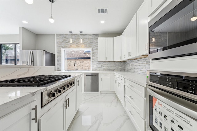 kitchen featuring light stone countertops, white cabinetry, hanging light fixtures, stainless steel appliances, and tasteful backsplash