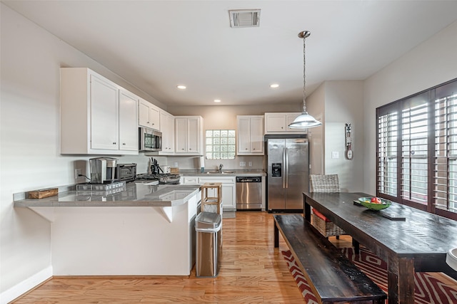 kitchen featuring white cabinetry, hanging light fixtures, stainless steel appliances, kitchen peninsula, and a breakfast bar