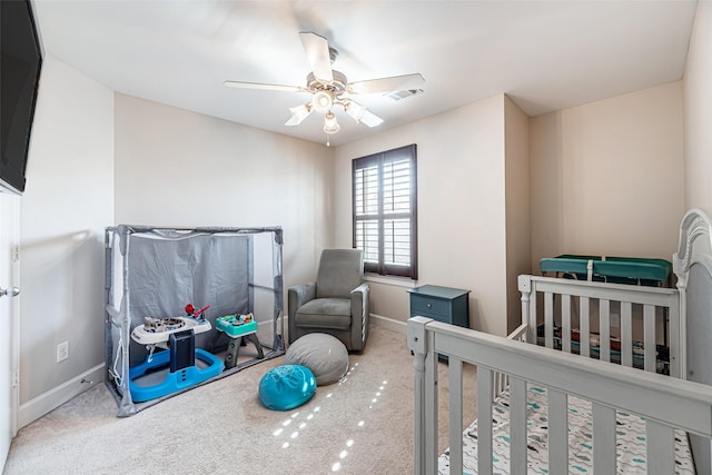 carpeted bedroom with ceiling fan and a crib