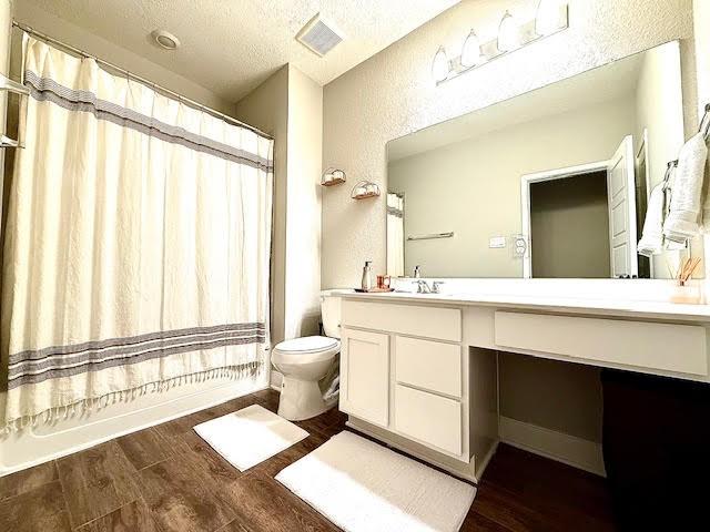 full bathroom featuring shower / bath combo, toilet, a textured ceiling, and vanity