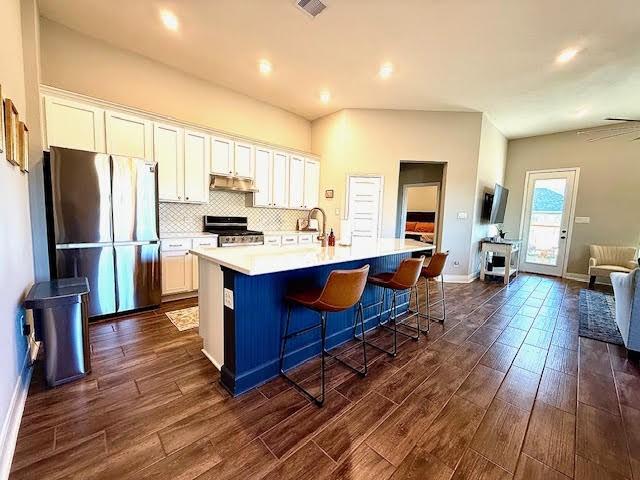 kitchen with appliances with stainless steel finishes, white cabinetry, a kitchen island with sink, and a kitchen breakfast bar