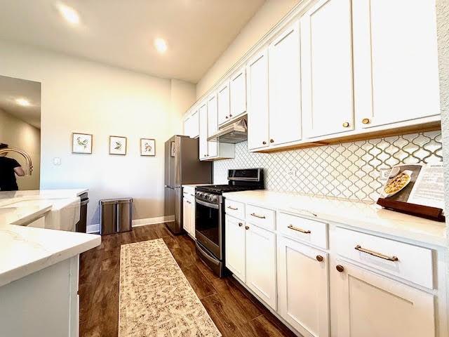 kitchen with light stone countertops, appliances with stainless steel finishes, dark hardwood / wood-style flooring, backsplash, and white cabinets