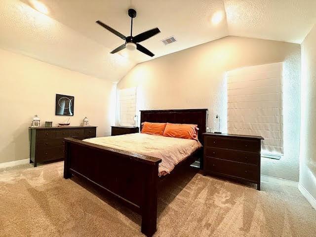 carpeted bedroom with a textured ceiling, vaulted ceiling, and ceiling fan